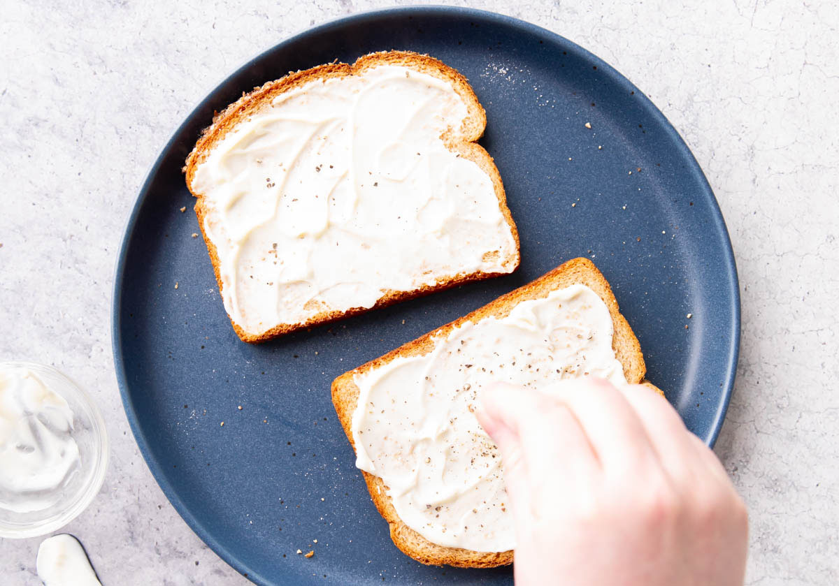 Hand sprinkling salt over mayonnaise on bread