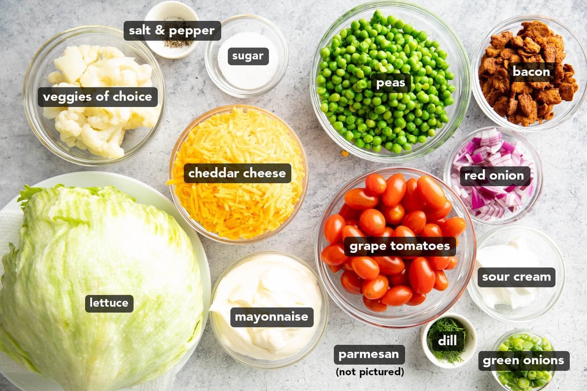 7 Layer Salad Ingredients pre-measured into glass bowls including peas, tomatoes, dressing, and bacon