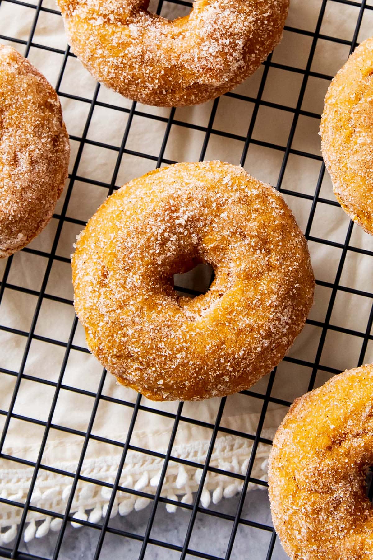 close up of baked pumpkin donuts that are moist and coated in cinnamon sugar on a cooling rack