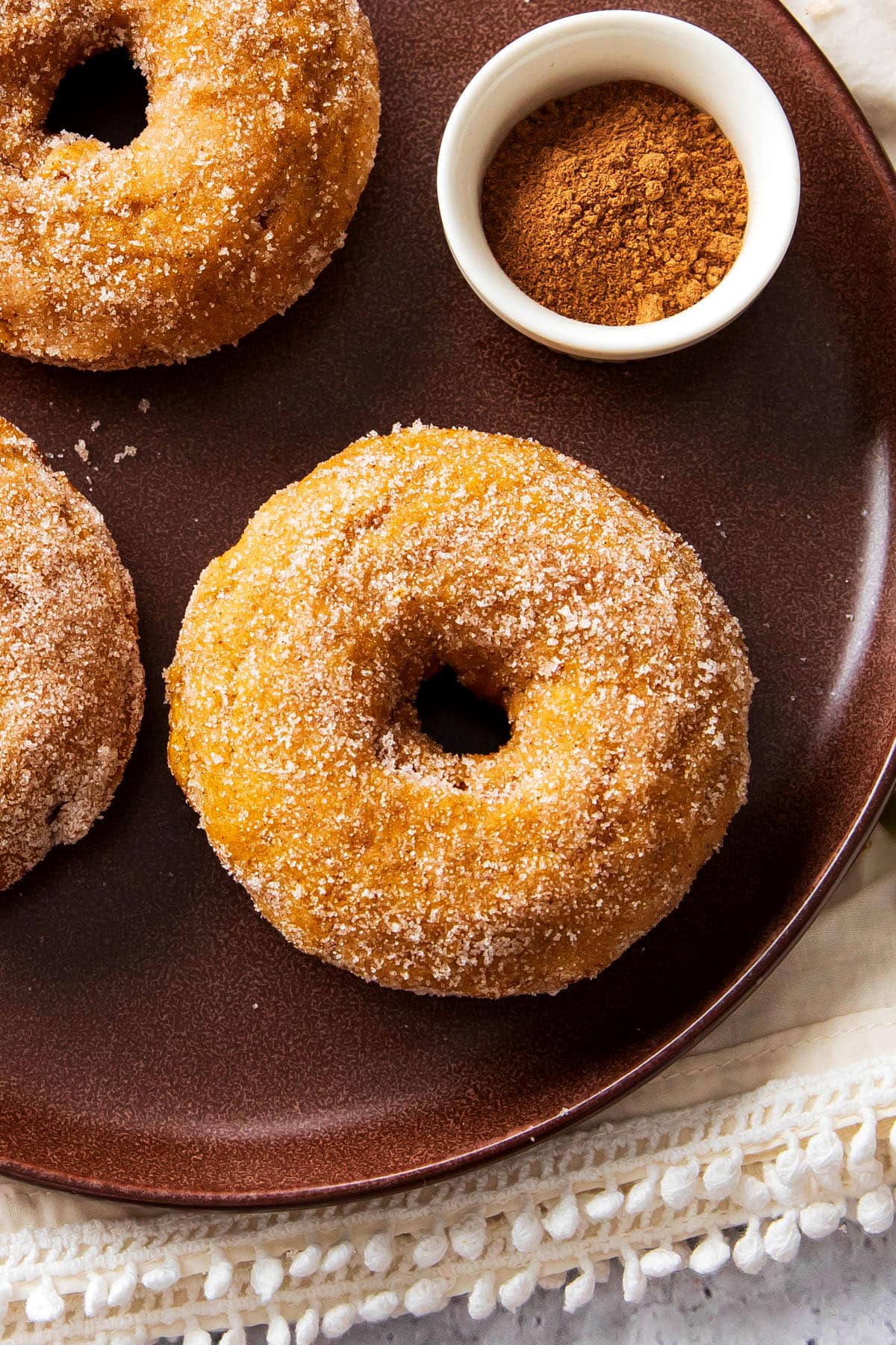 baked pumpkin donuts served on a plate with a cup of ground cinnamon and more doughnuts