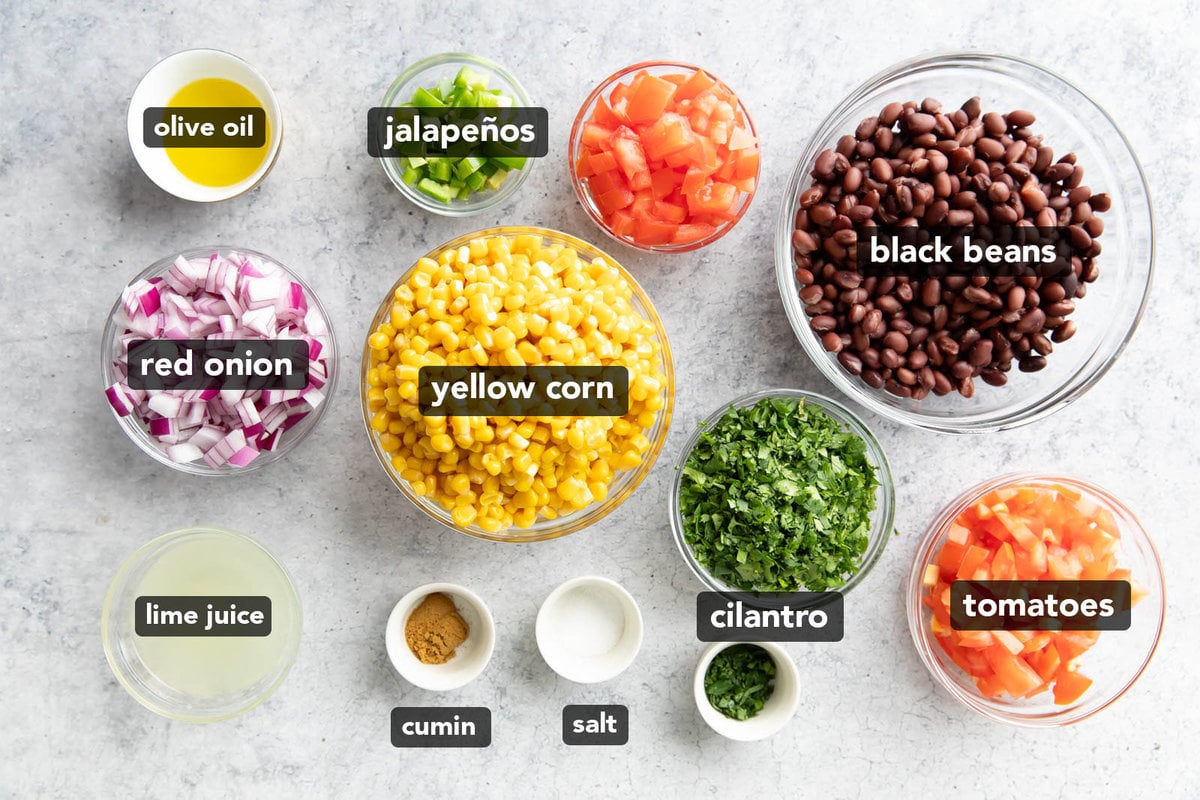 Black bean and corn salsa ingredients measured into prep bowls including red onions, black beans, corn, jalapeños, tomatoes, lime juice and salt.