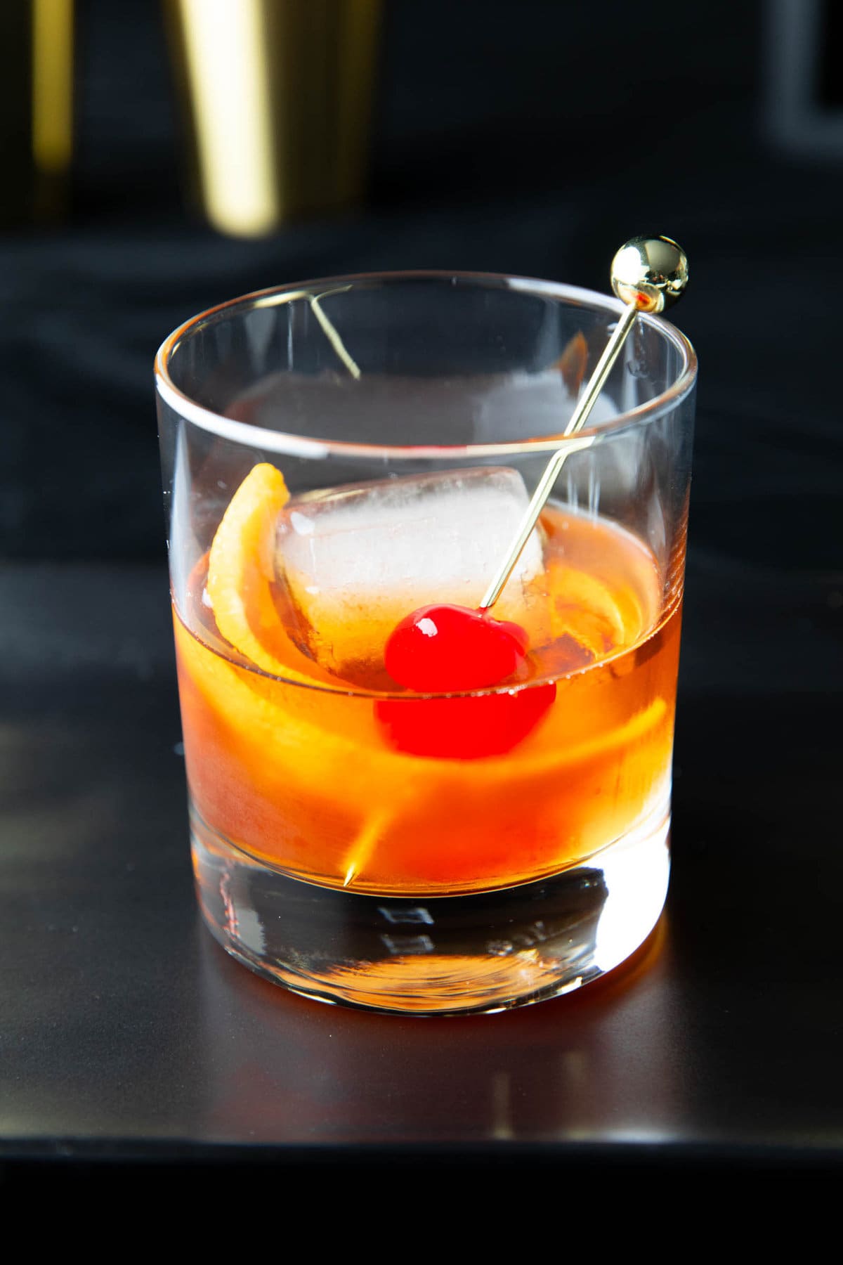 close up of this whiskey cocktail garnished with an orange peel and a maraschino cherry