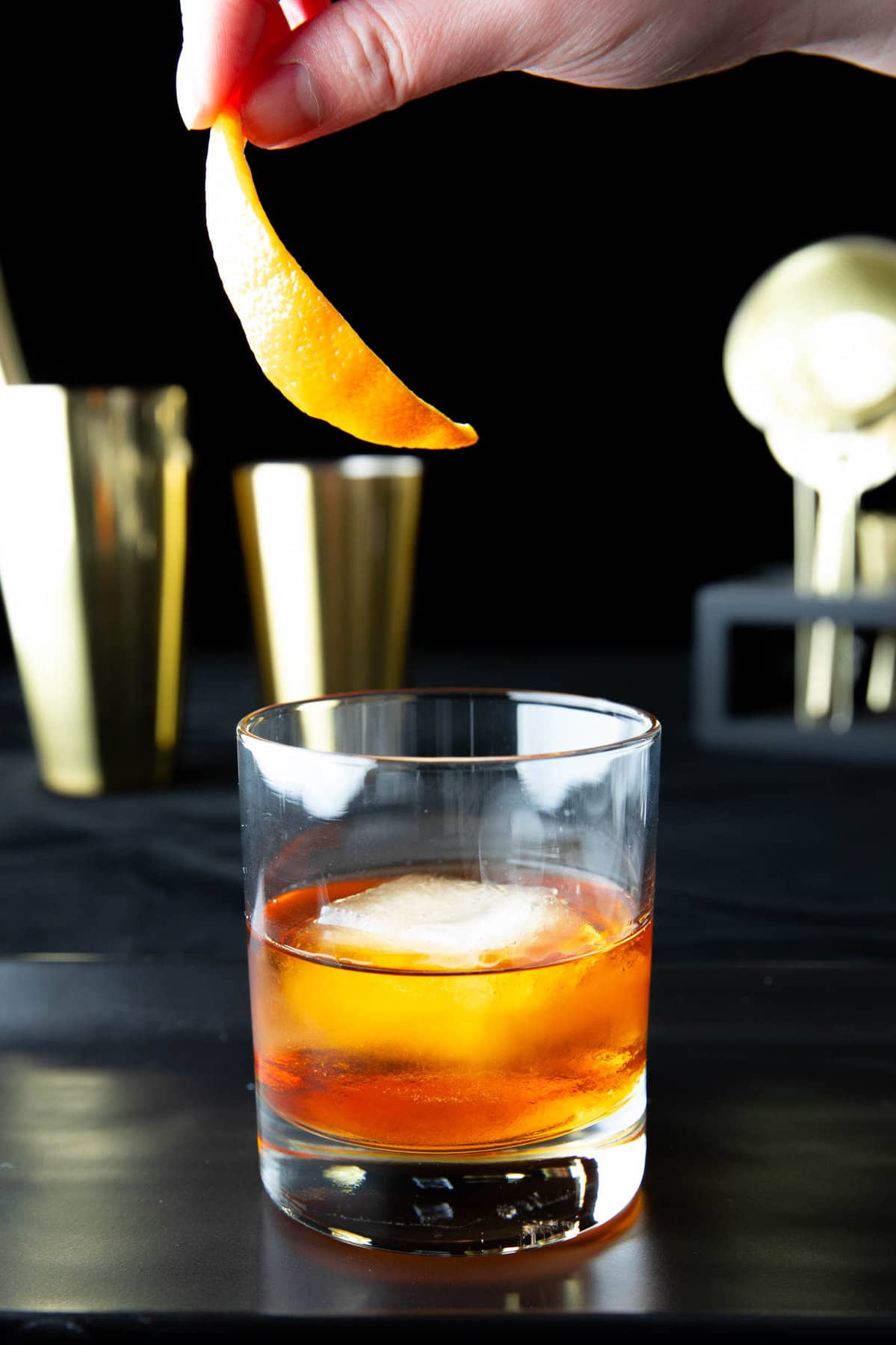 A hand adding an orange peel garnish to this Old Fashioned drink recipe