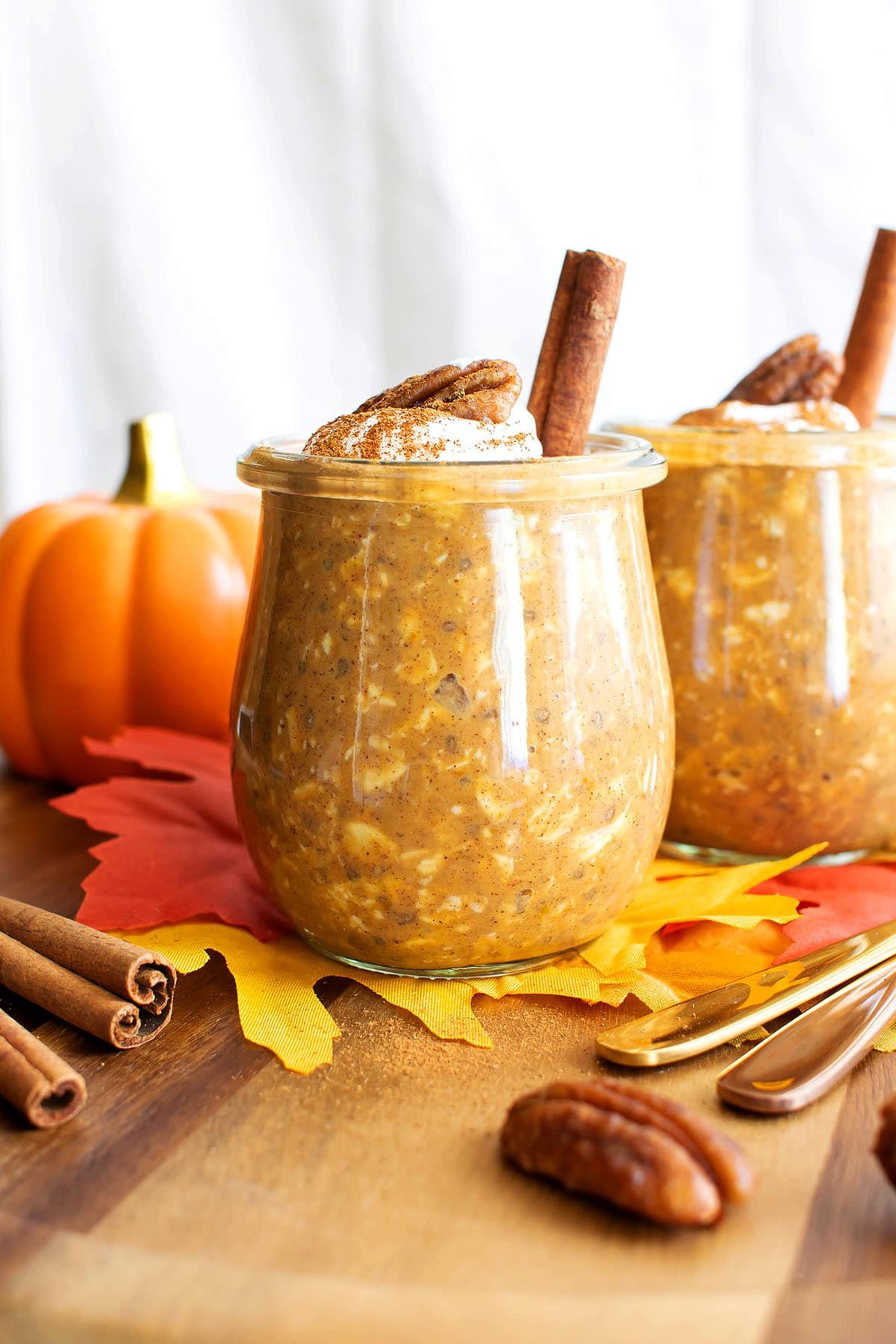 Two jars of pumpkin overnight oats are served on a fall breakfast table with pumpkins and leaves.