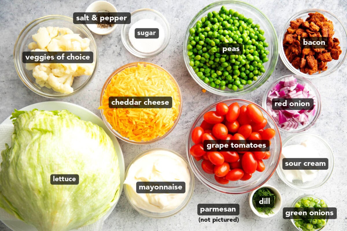 Traditional 7 Layer Salad Ingredients pre-measured into glass bowls including peas, tomatoes, dressing, and bacon.