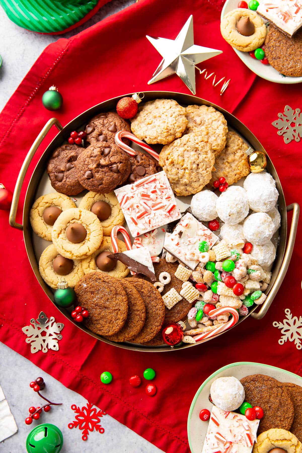 A golden tray filled with Christmas Treats such as peppermint bark, peanut butter blossoms, and snowball cookies.