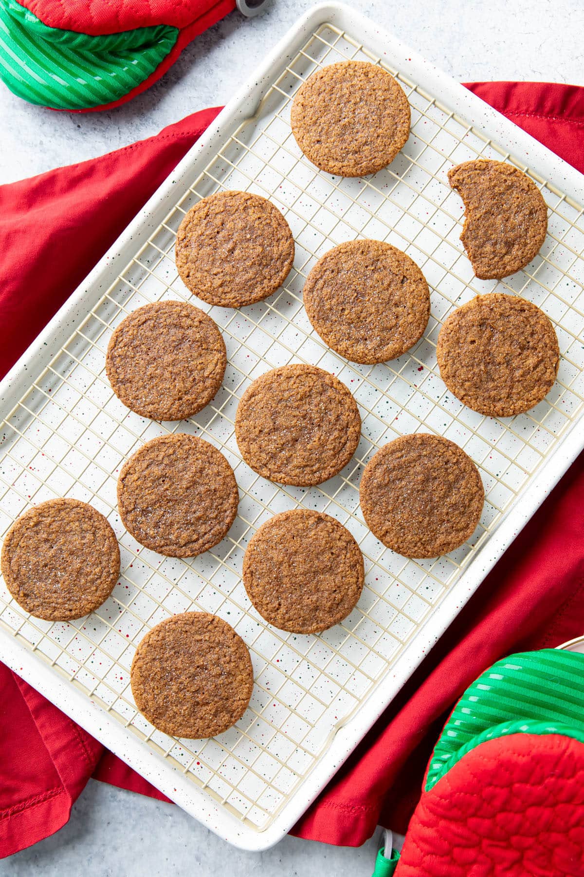 Gingersnap cookies on a cooling rack placed inside of a baking sheet with one cookie bitten