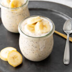 Two jars of banana overnight oats served with banana slices and spoons
