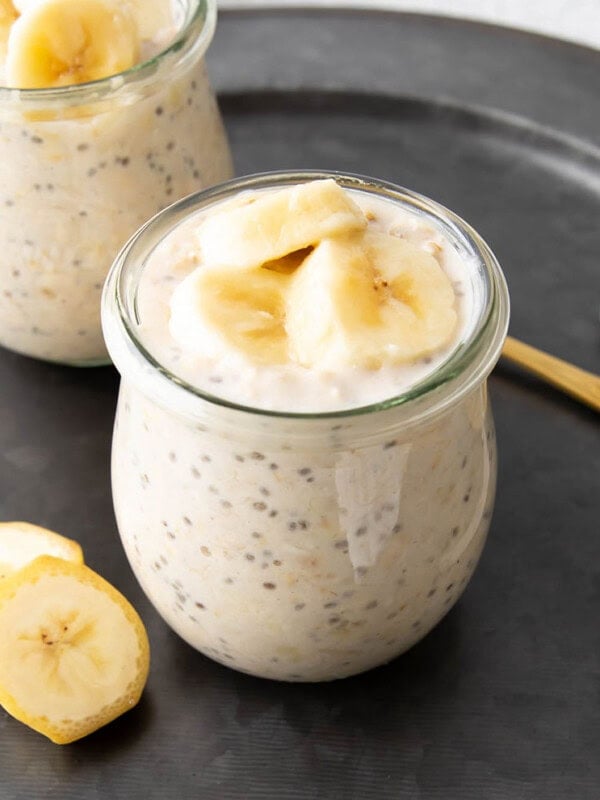 Two jars of banana overnight oats served with banana slices and spoons