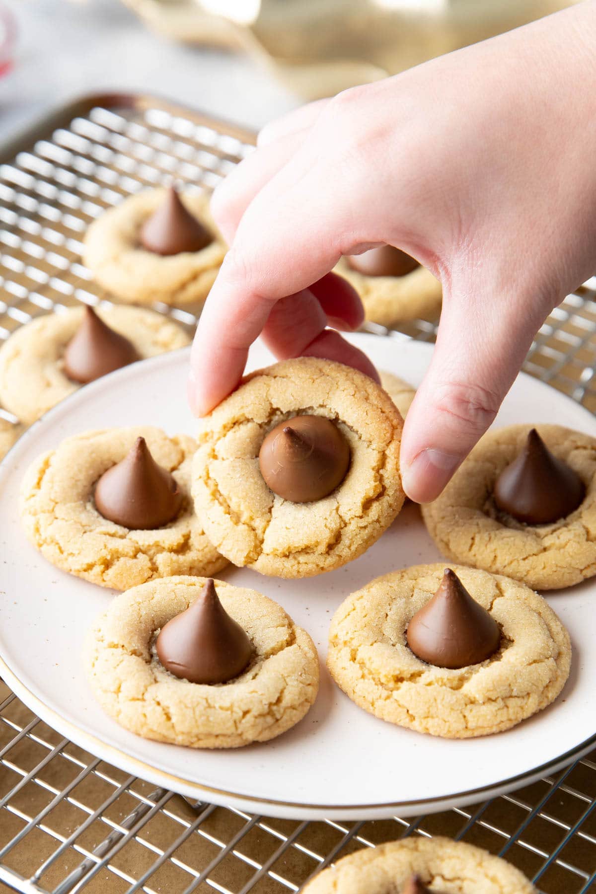 Hand picking up a peanut butter blossom cookie from a plate