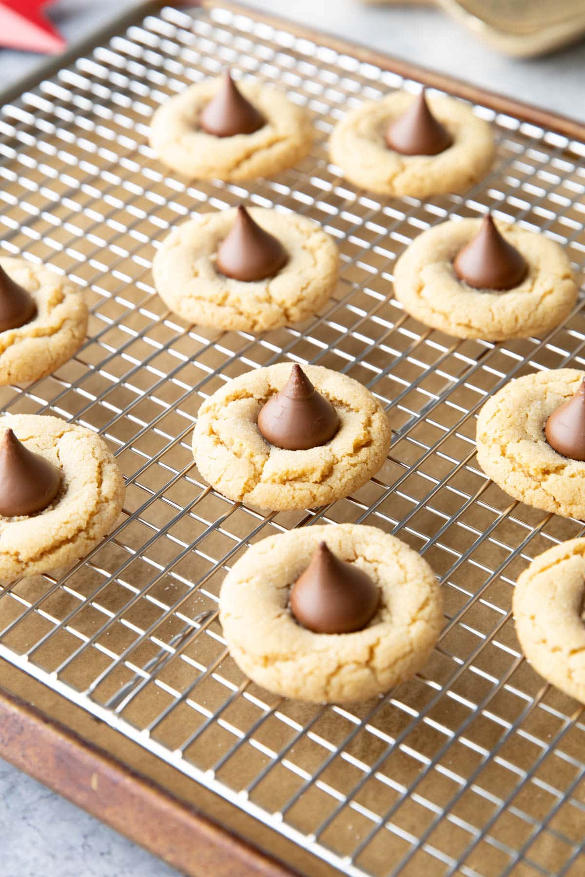 Peanut Butter Blossoms arranged evenly spaced apart on a silver cooling rack placed over a baking sheet