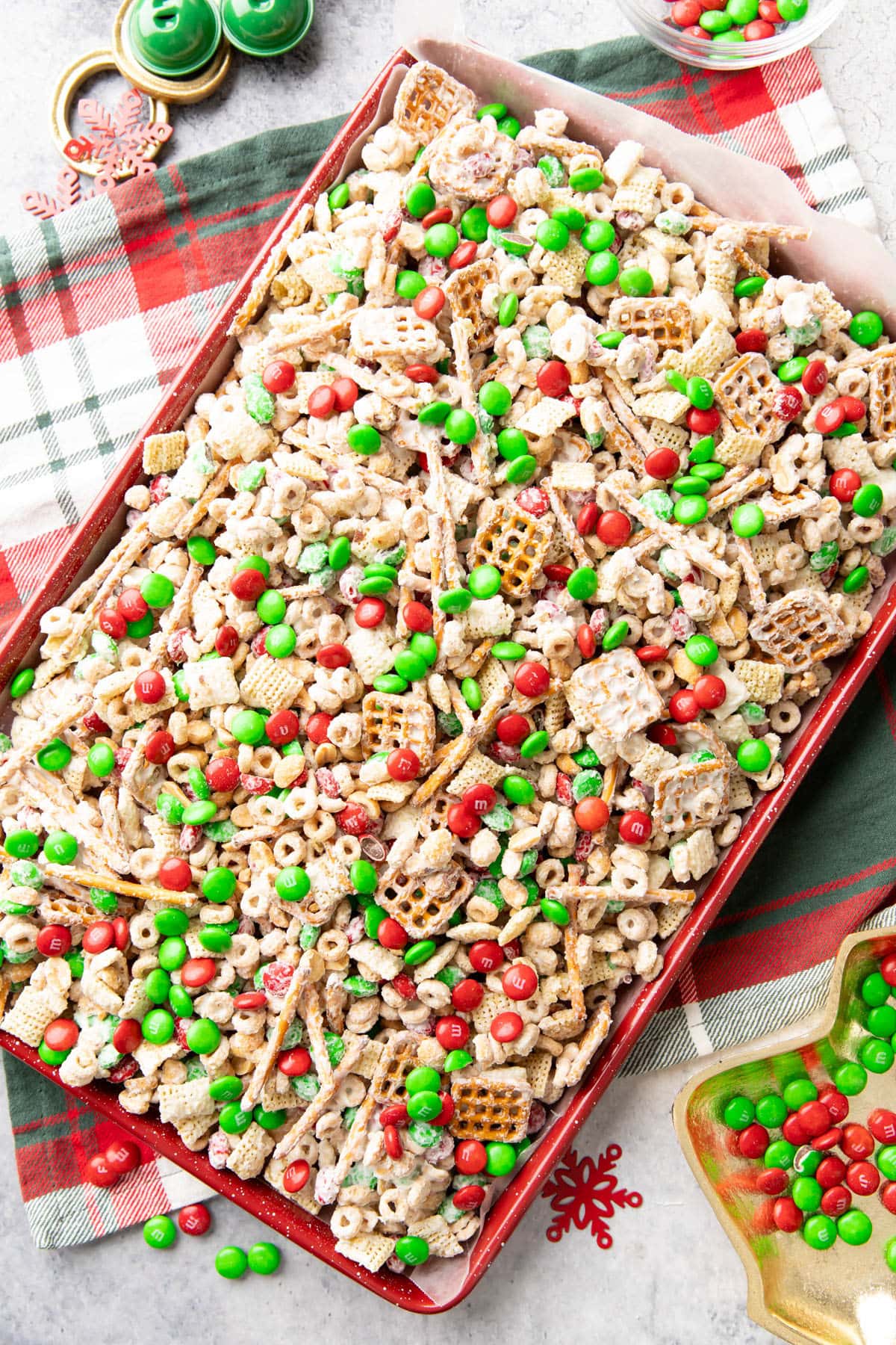 Christmas snack mix complete, with white chocolate coating, chocolate candies, pretzels, cheerios, rice chex, and holiday decorations in gold, green, and red