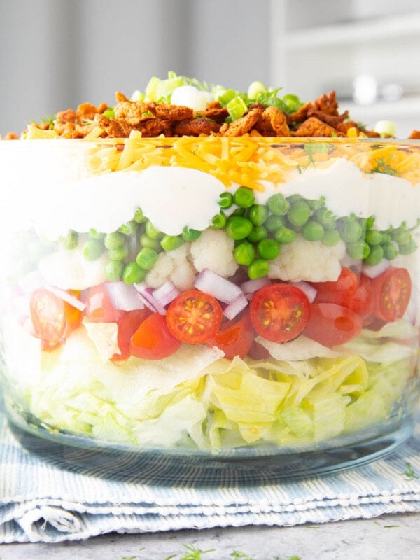 A 7 Layer Salad served in a glass bowl to showcase layers of lettuce, bacon, cheddar cheese, and salad dressing