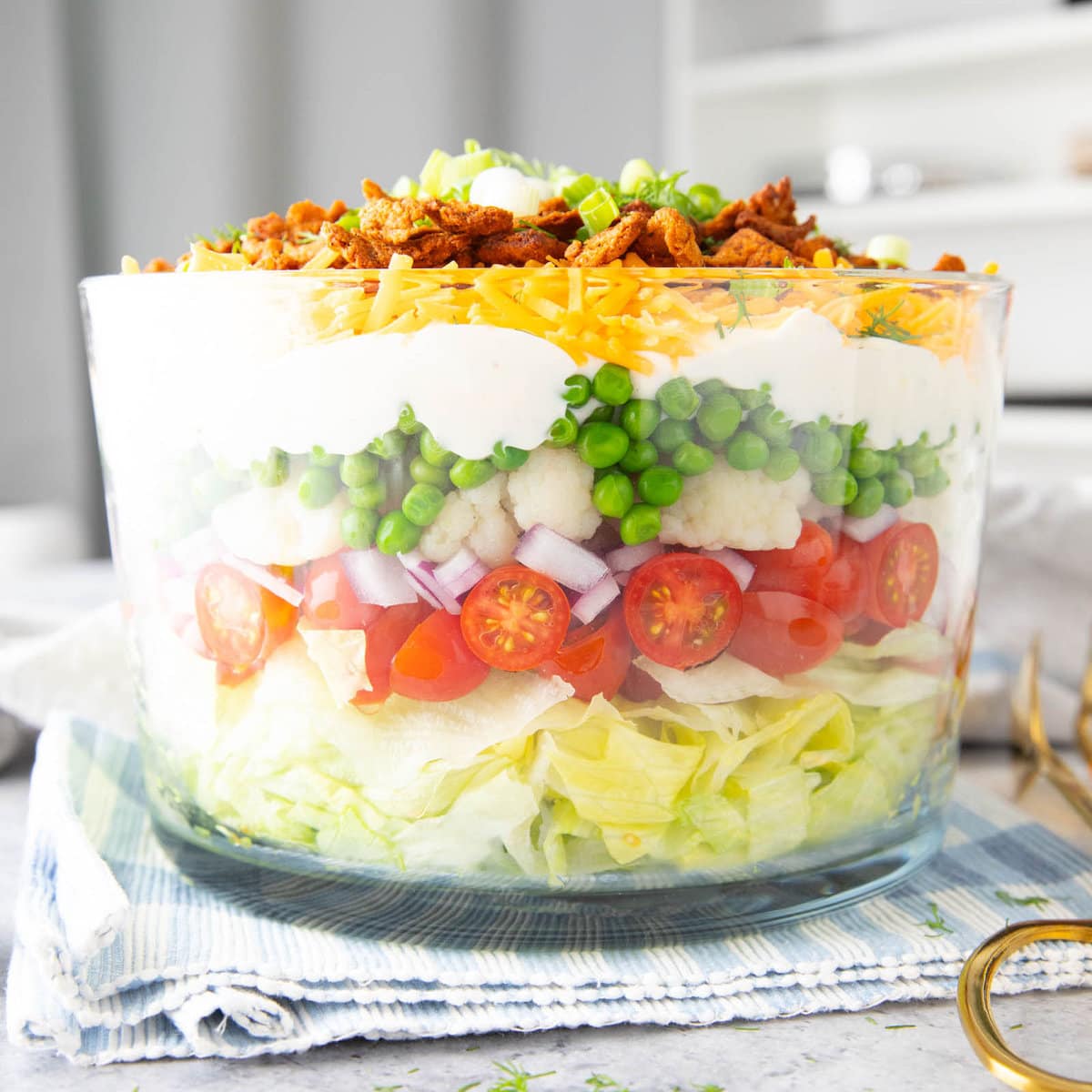A 7 Layer Salad served in a glass bowl to showcase layers of lettuce, bacon, cheddar cheese, and salad dressing