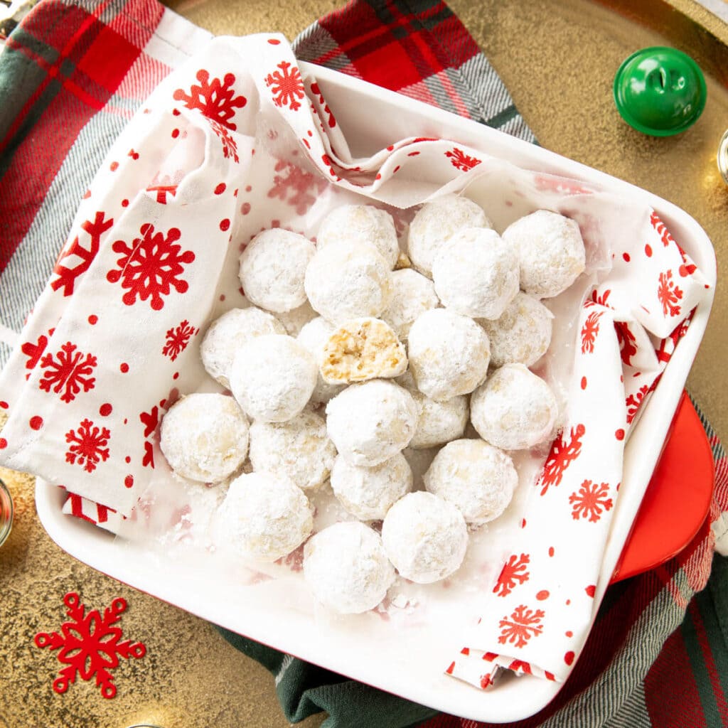Square photo of snowball cookies in a serving platter with a holiday napkin