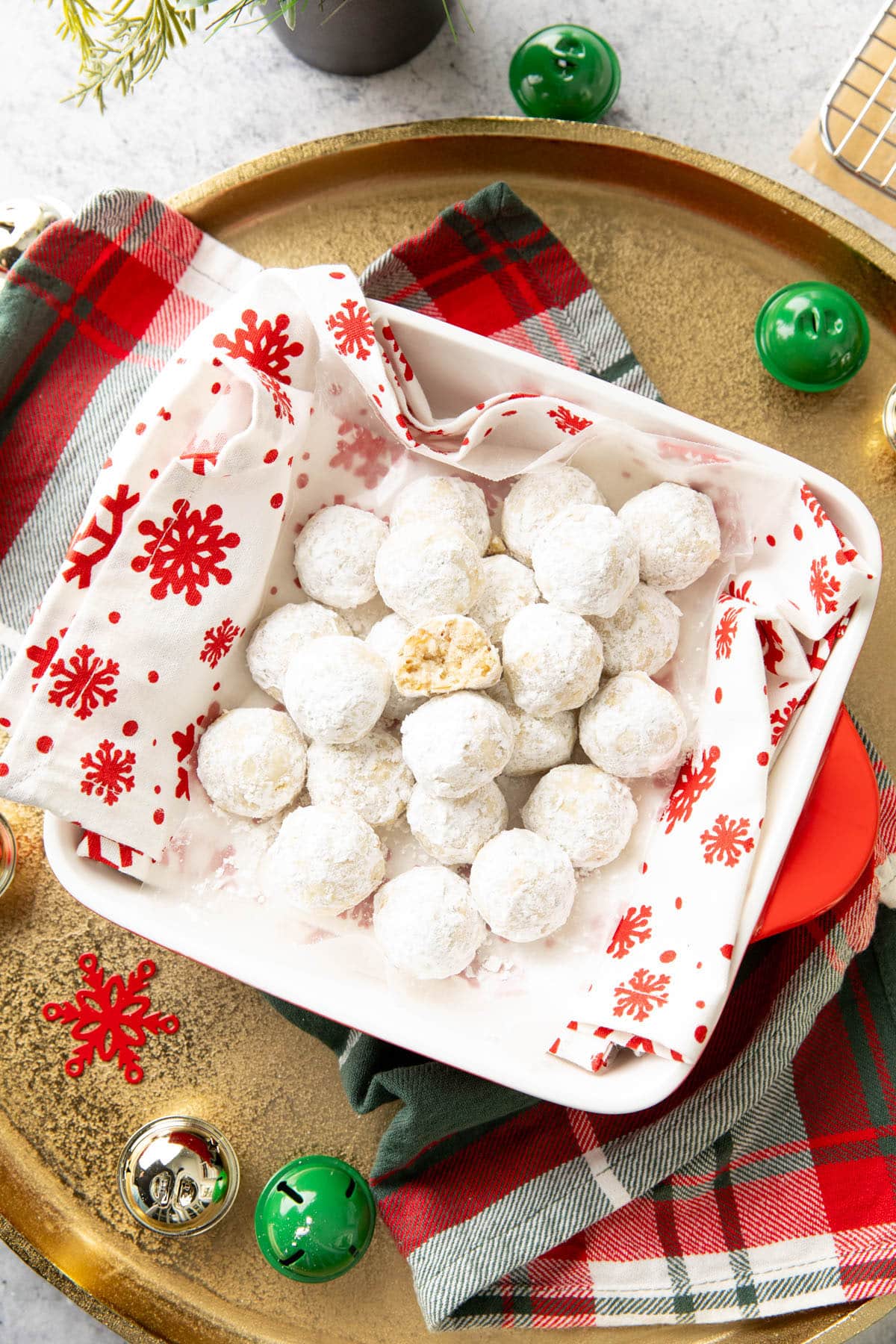 Overhead photo of snowball cookies wrapped red snowflake napkin on a gold tray