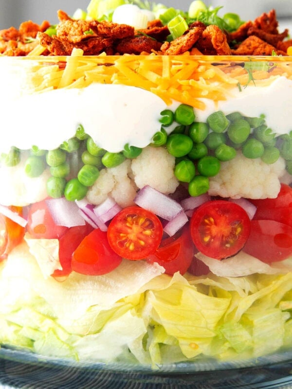 close up of Seven Layer salad to showcase layers, including peas, cauliflower, red onions, tomatoes, mayonnaise dressing, cheese, and bacon