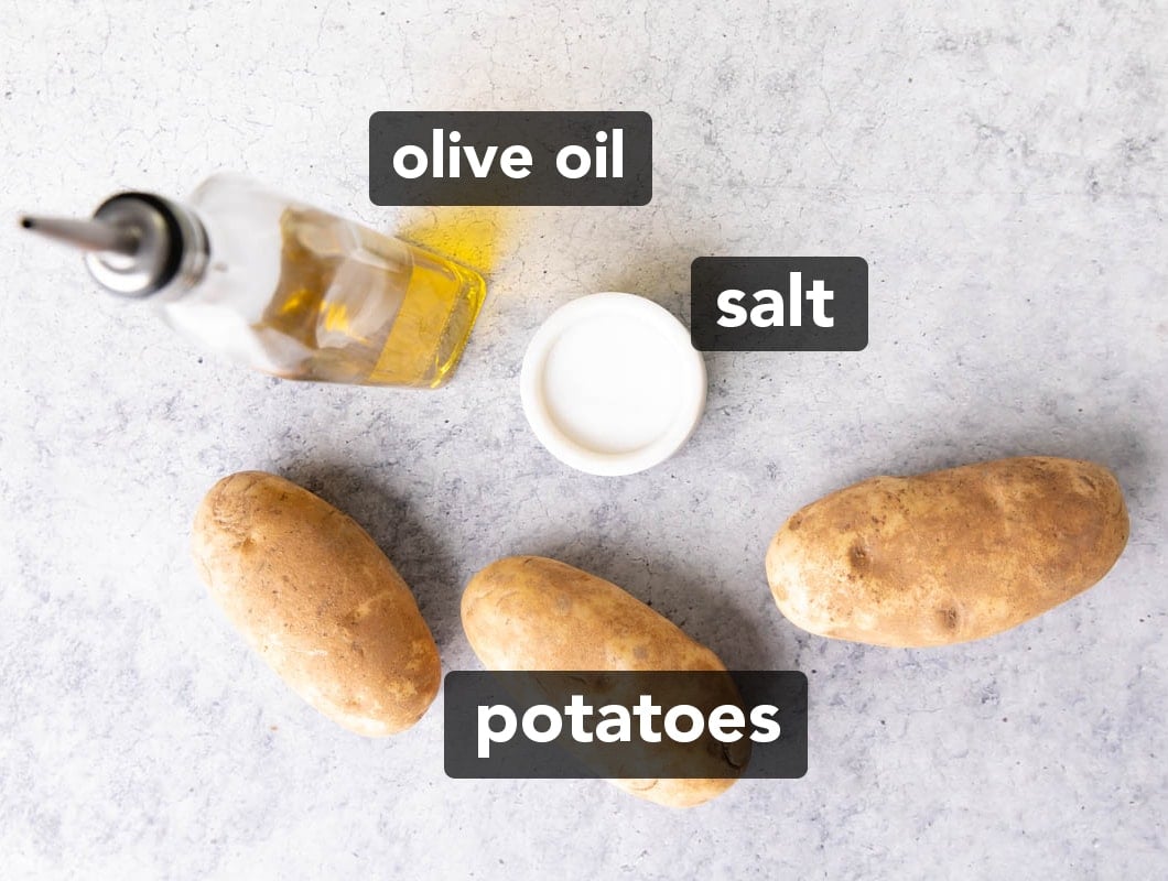 Air fryer French fries ingredients on a table including russet potatoes, olive oil, and salt.