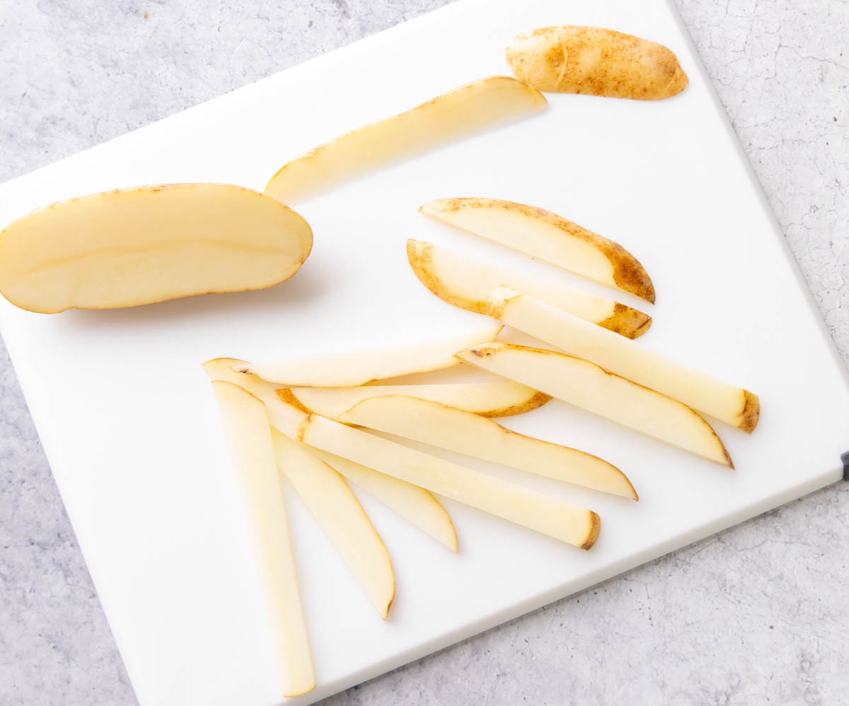 Washed and scrubbed potatoes on a cutting board with some sliced into ¼-inch thick slices to make air fryer fries.
