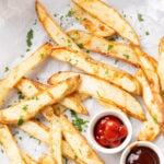 Air fryer french fries with crisped, browned edges sprinkled with parsley and served with ketchup and barbecue sauce