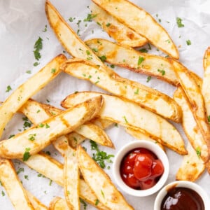 Air fryer french fries with crisped, browned edges sprinkled with parsley and served with ketchup and barbecue sauce