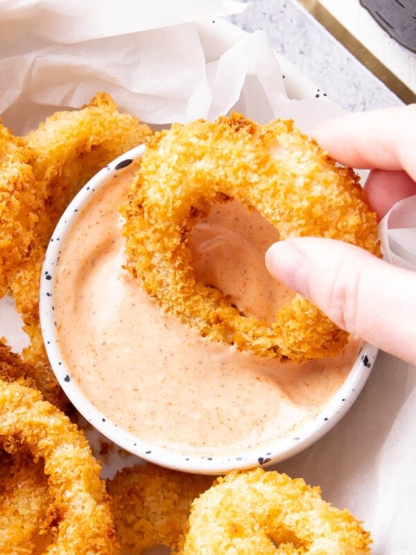 Hand dipping an onion ring into a bowl of onion ring sauce