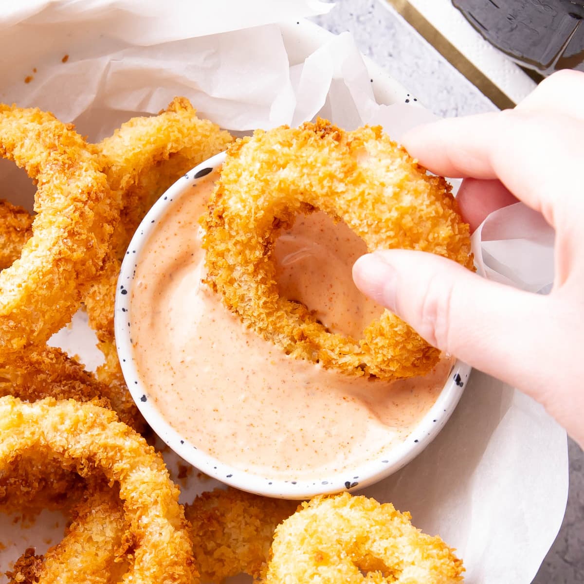 Hand dipping an onion ring into a bowl of onion ring sauce