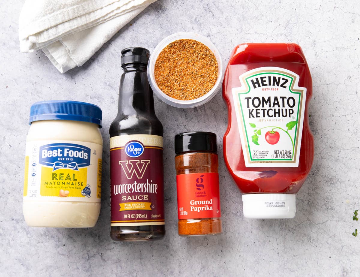 Onion Ring Sauce ingredients including a bottle of tangy mayonnaise, Worcestershire sauce, homemade Cajun seasoning, ground paprika, and delicious ketchup laid out on a table with labels.