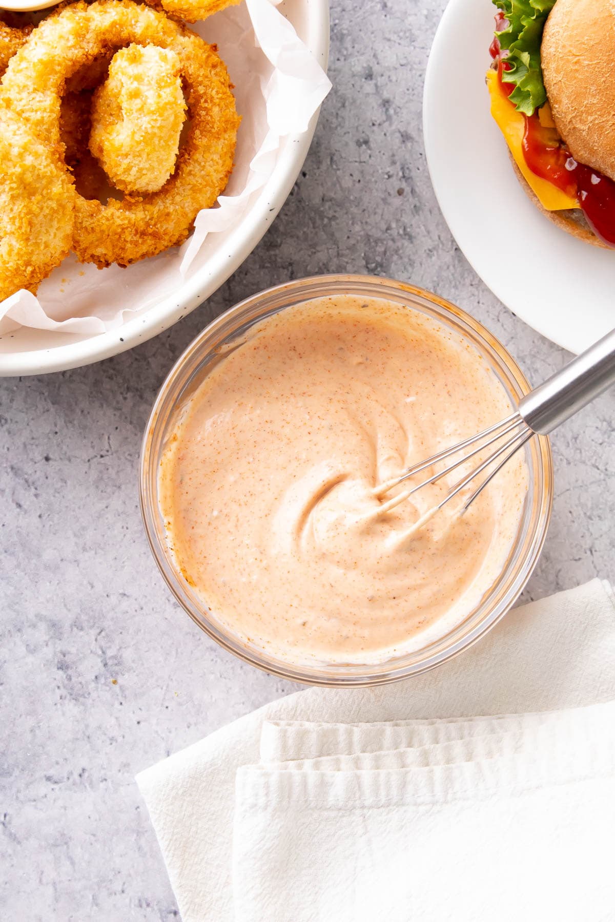 Creamy, thick homemade dip in a glass bowl with a whisk in it, served with sides and a burger