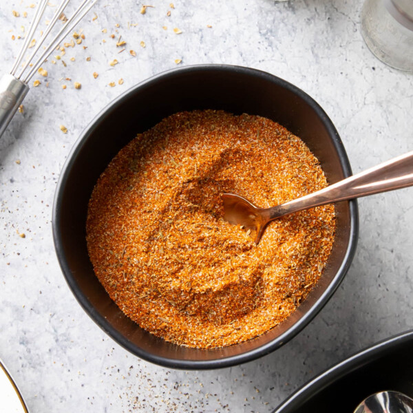 bowl of cajun seasoning with a spoon in it and spices on the table