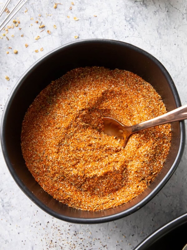 bowl of cajun seasoning with a spoon in it and spices on the table