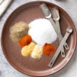 Individual spice ingredient for making Seasoned Salt measured and neatly laid out on a plate with measuring spoons