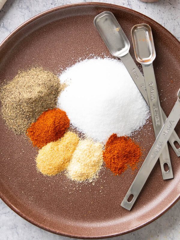 Individual spice ingredient for making Seasoned Salt measured and neatly laid out on a plate with measuring spoons