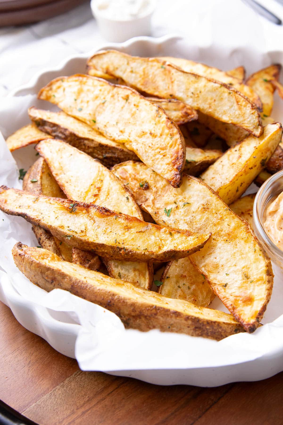 A platter of potato wedges made in the air fryer served with condiments and topped with seasonings.