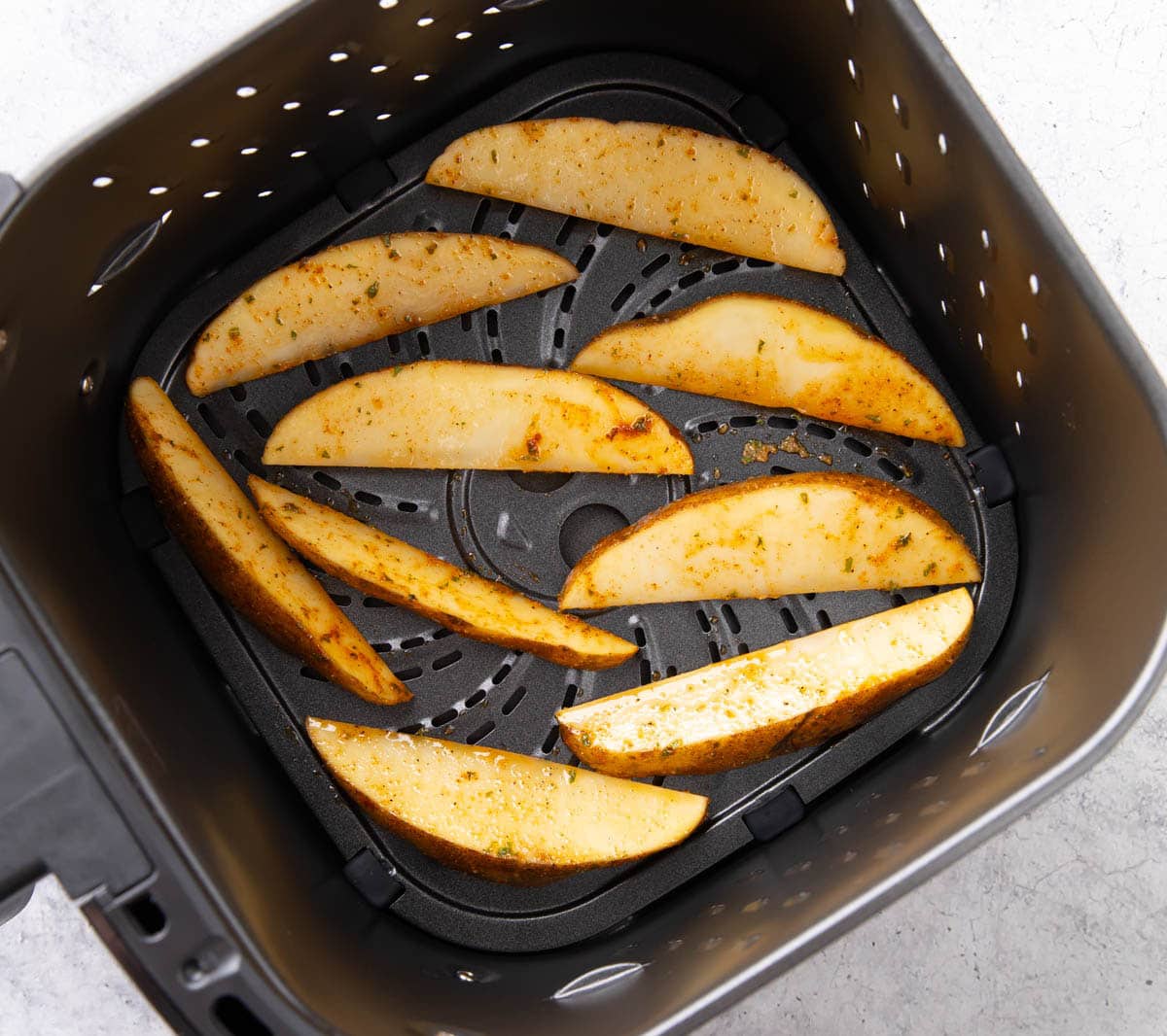 Potato wedges in air fryer laid out in a single, spaced out layer to avoid crowding to cook evenly.