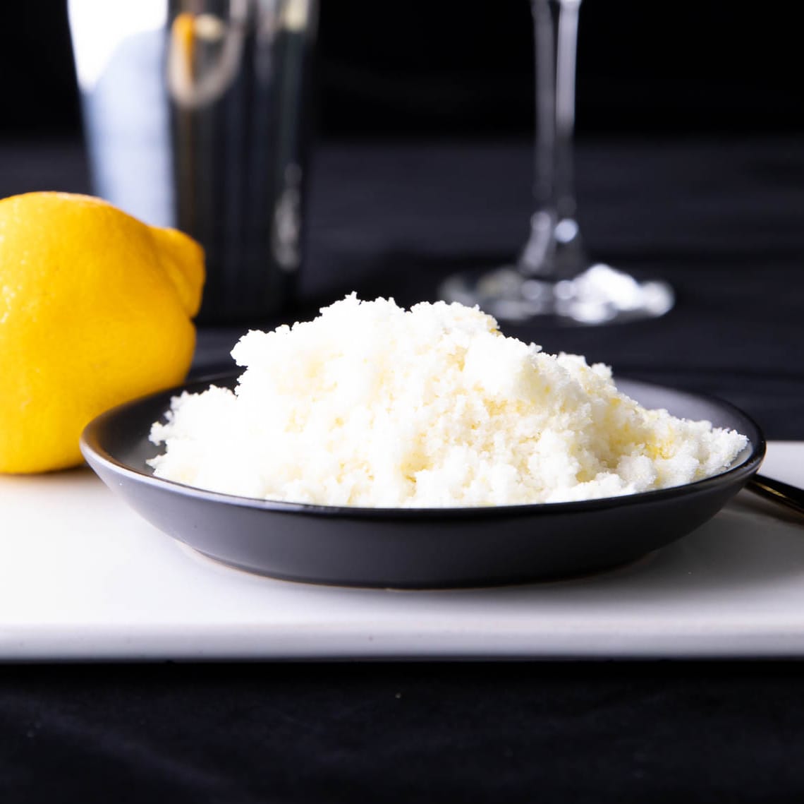 Plate full of lemon sugar served with a lemon and a cocktail set.