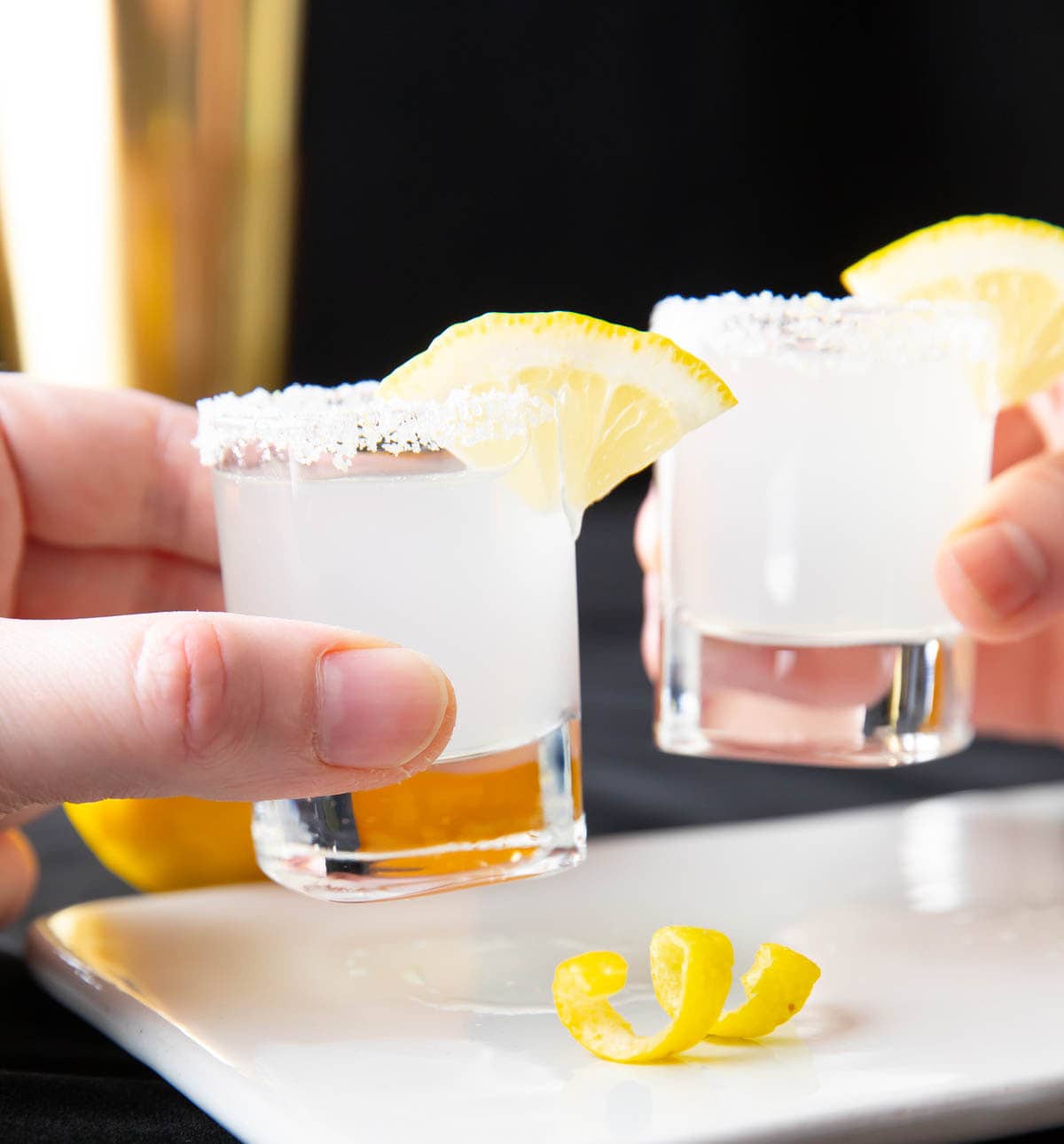 Two hands holding lemon drop shots and cheering