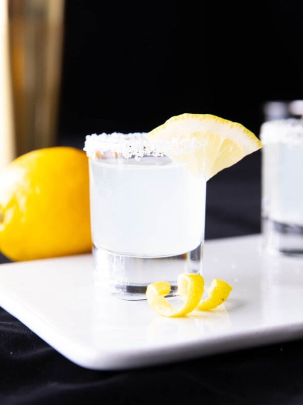 Two photos showing how to make a lemon drop shot - straining shot mixture into a sugared rim shot glass