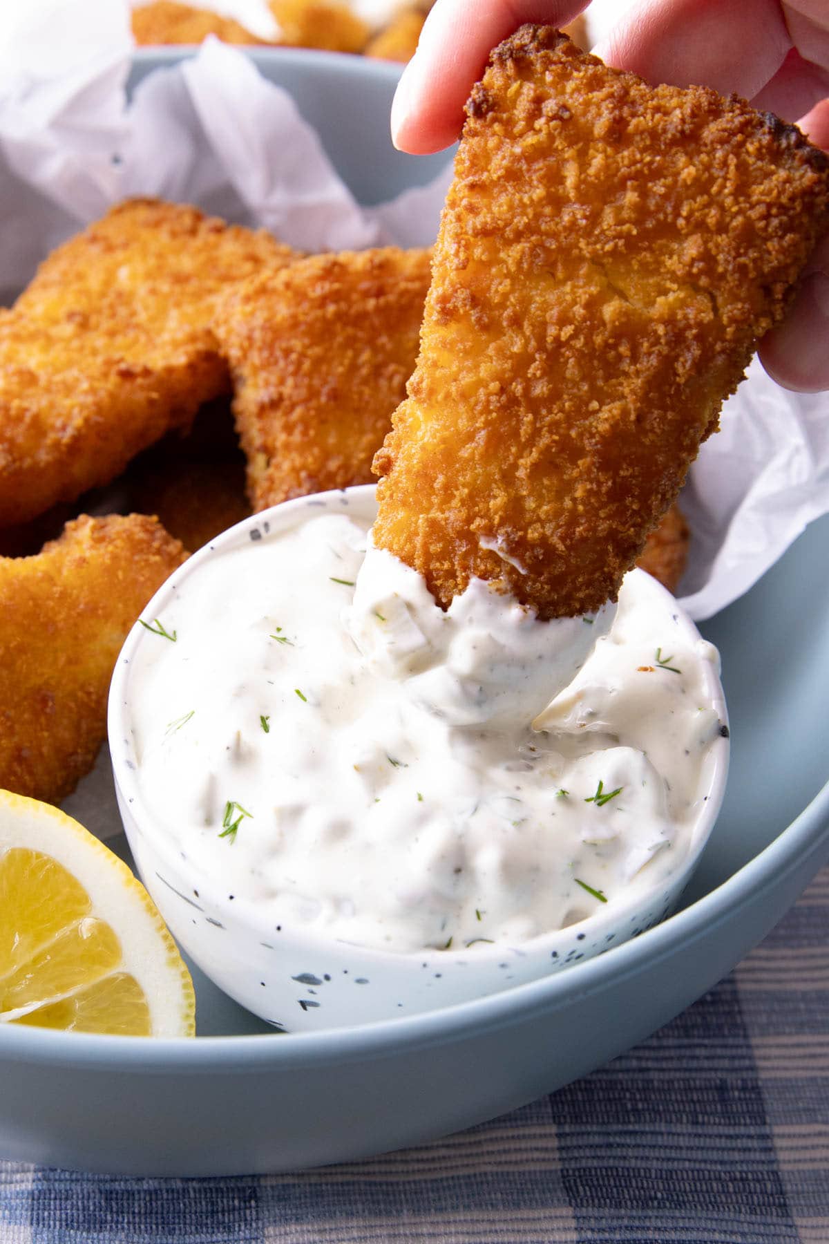 Dipping a fish stick into a bowl of creamy tartar sauce thick with chopped dill pickles and lemon juice