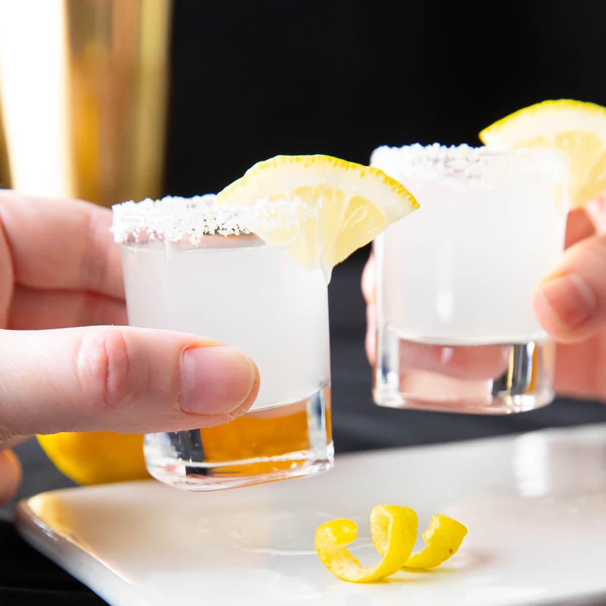 Two hands holding lemon drop shots and cheering