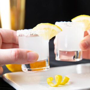 two hands clinking shot glasses full of lemon drop shots