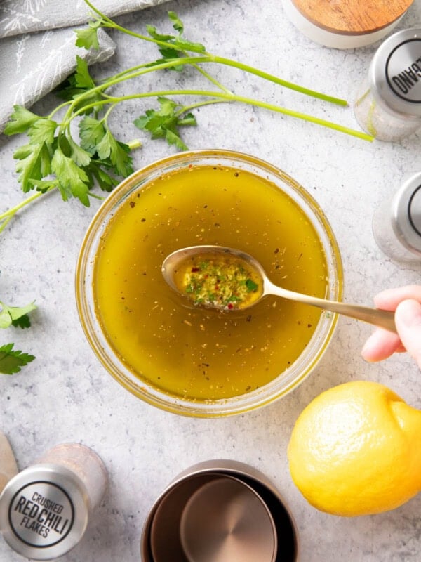 Spooning this Italian Dressing Recipe from a mixing bowl to showcase the ingredients, including herbs, olive oil, lemon juice, and more.