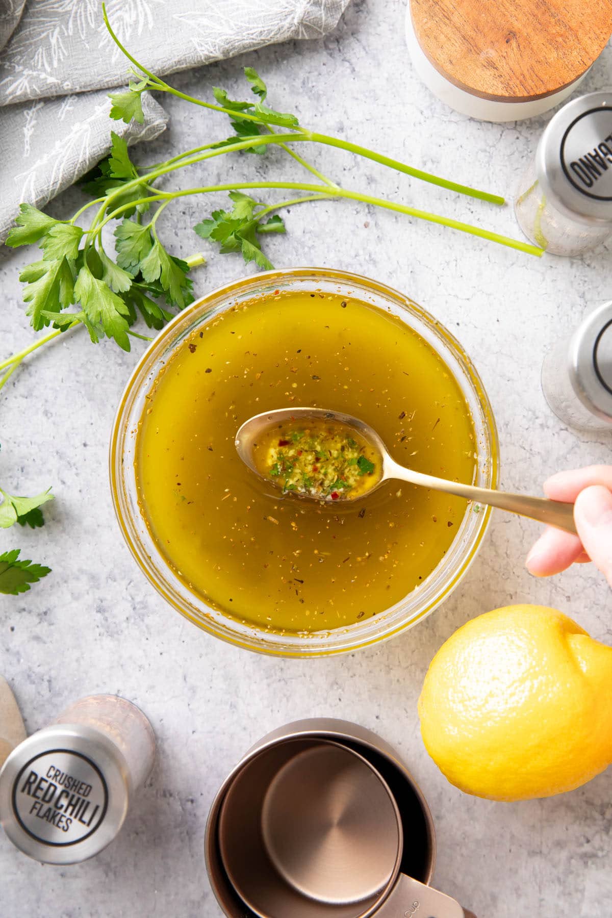 Spooning this Italian Dressing Recipe from a mixing bowl to showcase the ingredients, including herbs, olive oil, lemon juice, and more.