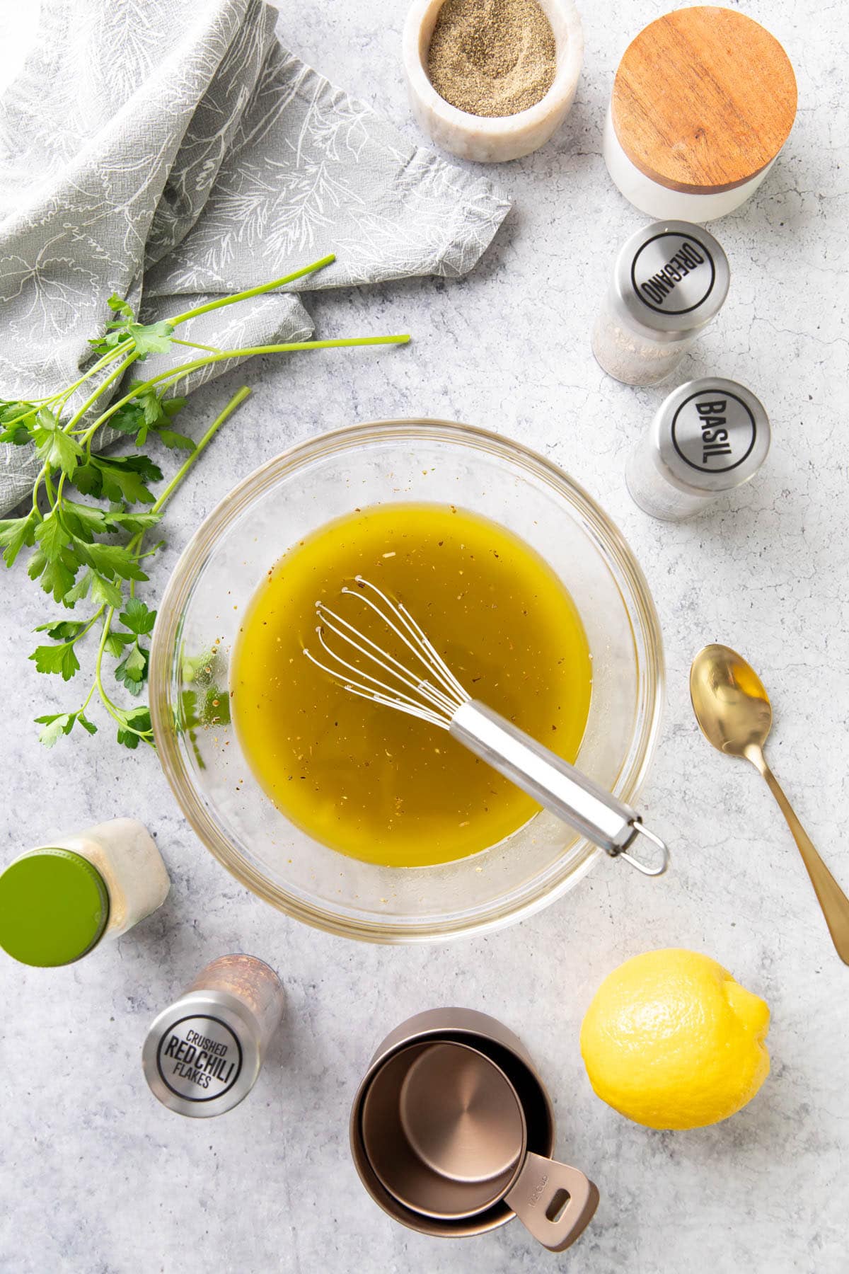 Kitchen table covered in Italian dressing ingredients, including a lemon, dried basil, salt, pepper, and red chili flakes