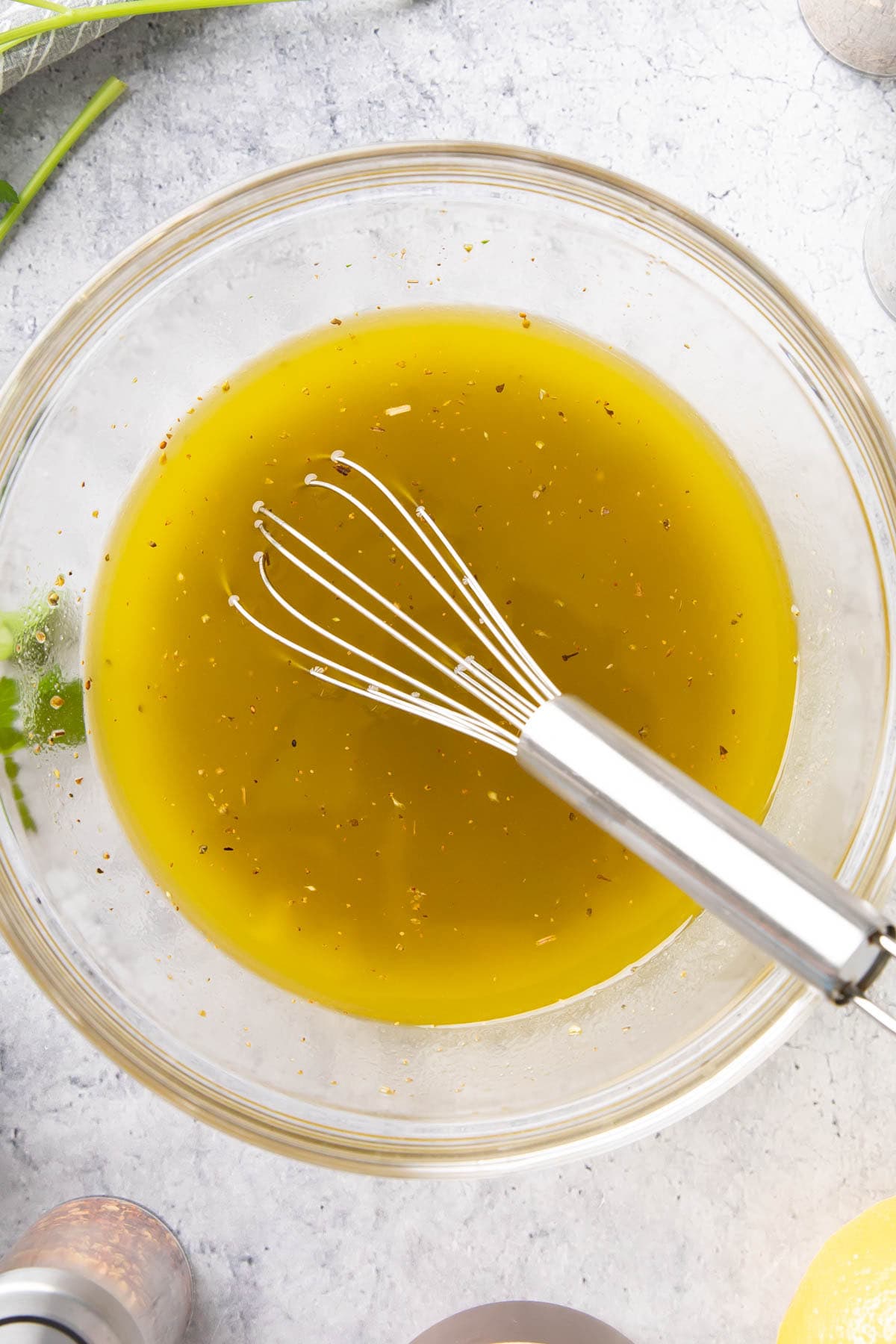 a whisk sitting in a bowl of this salad addition packed with oil, white wine vinegar, lemon juice, and herbs