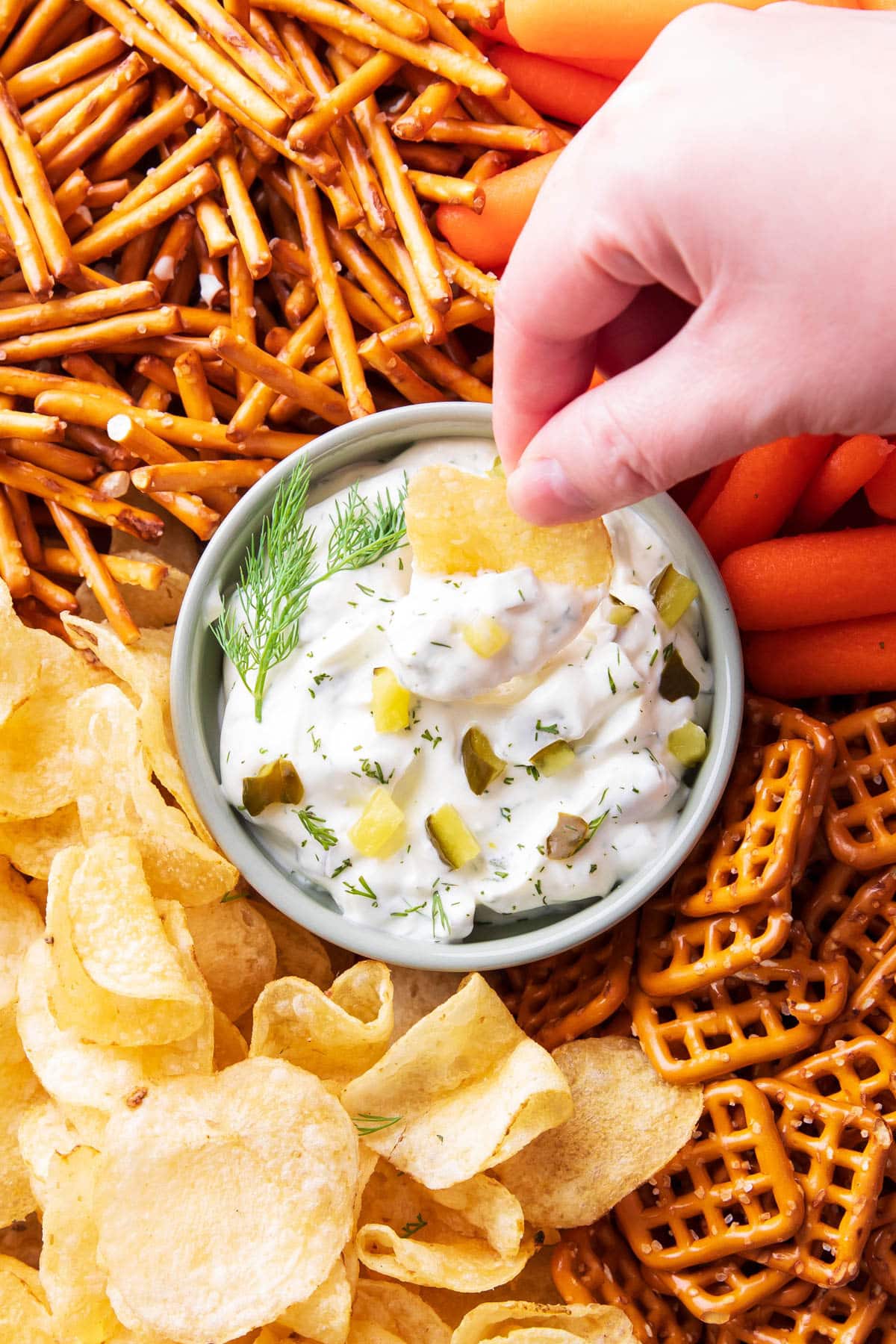 Dipping a crisp potato chip into this homemade condiment in a bowl topped with pickles and herbs.