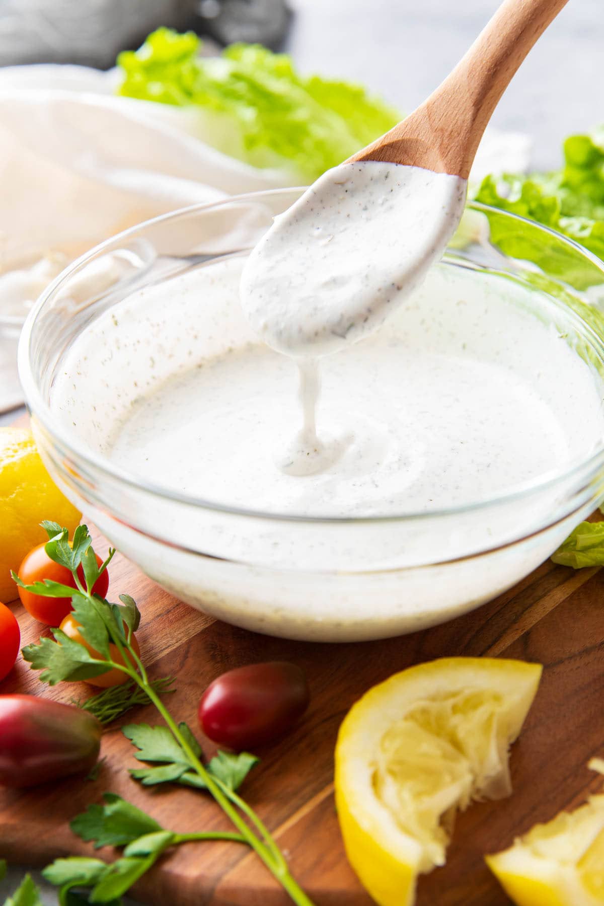 Drizzling this homemade salad sauce into a bowl surround by lettuce, lemons, tomatoes, and more.