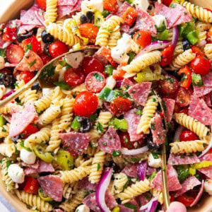 A large serving bowl filled with Italian pasta salad featuring juicy tomatoes, fresh parsley, flavorful salami, mozzarella pearls, bell peppers, and delicious Italian dressing.