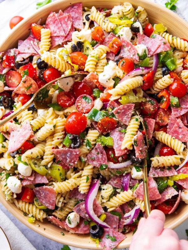 A large serving bowl filled with Italian pasta salad featuring juicy tomatoes, fresh parsley, flavorful salami, mozzarella pearls, bell peppers, and delicious Italian dressing.