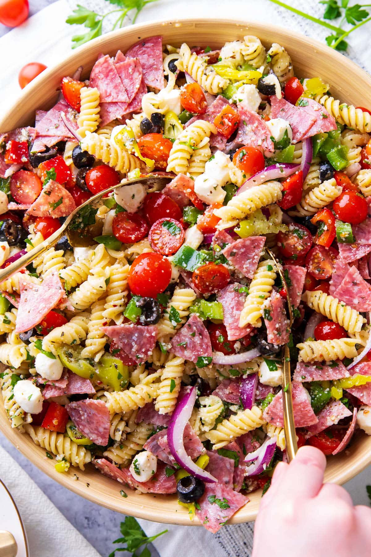 A large serving bowl filled with Italian pasta salad featuring juicy tomatoes, fresh parsley, flavorful salami, mozzarella pearls, bell peppers, and delicious Italian dressing